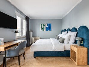 A modern hotel room with a bed, a desk, and a chair. There is a TV mounted on the wall and artwork on the wall. - Numa Düsseldorf Artol (Düsseldorf)