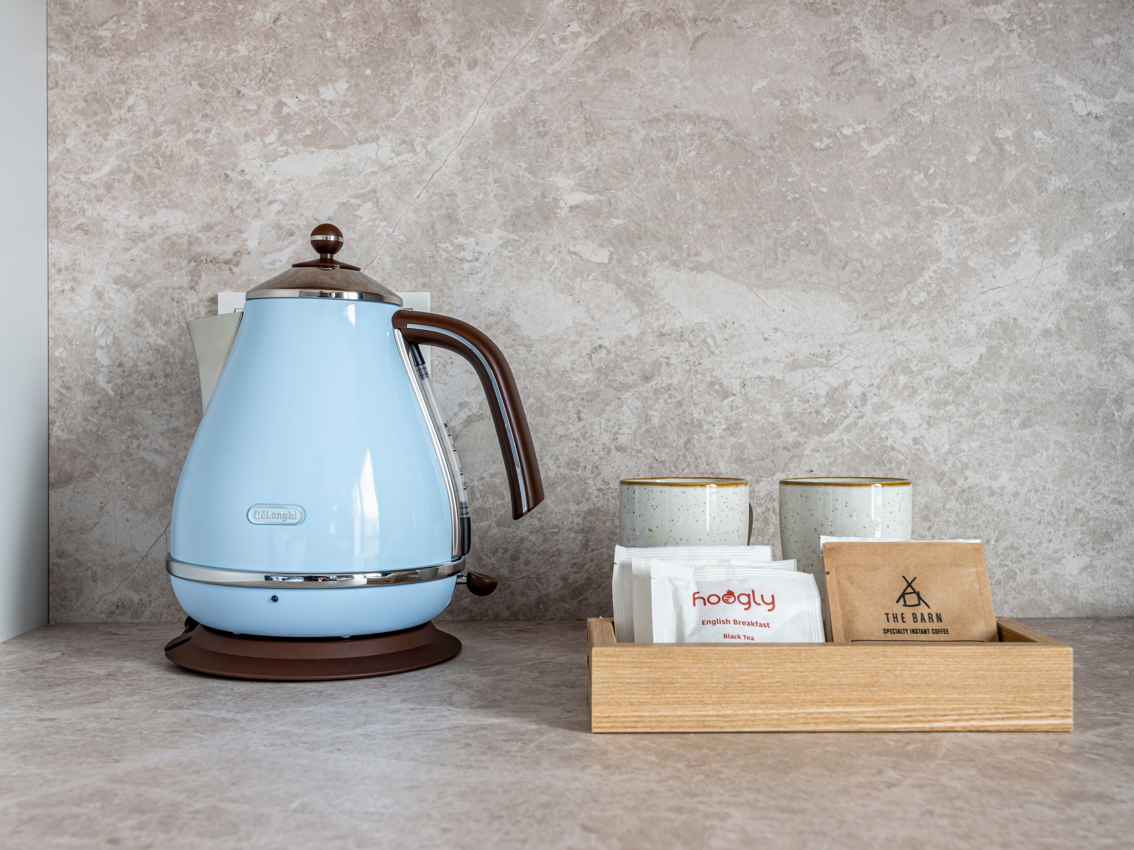 Una tetera azul sobre una encimera con dos tazas de café y una caja de café envasado.