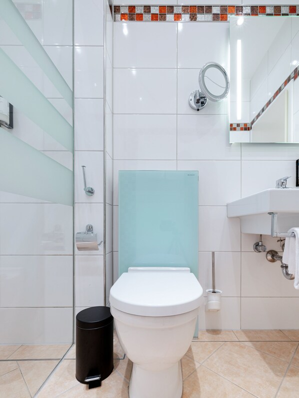 A modern bathroom with a white toilet, a glass shower enclosure, and a white sink with a mirror above it. - Numa Düsseldorf Artol (Düsseldorf)
