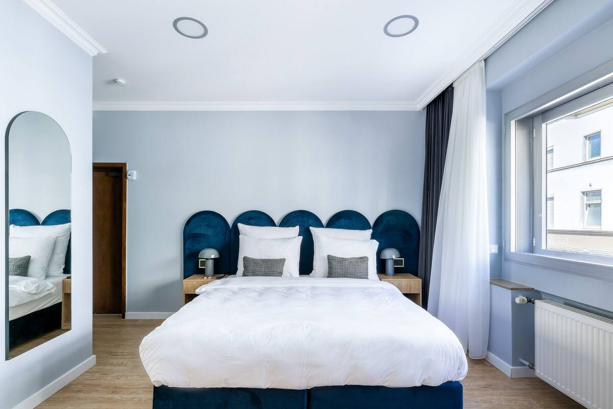 Une chambre moderne avec un grand lit, un miroir et une fenêtre avec des rideaux.