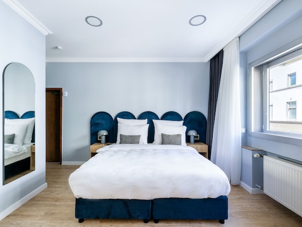 Relax in a spacious room with a large bed, a mirror, and a window offering a view of the city.