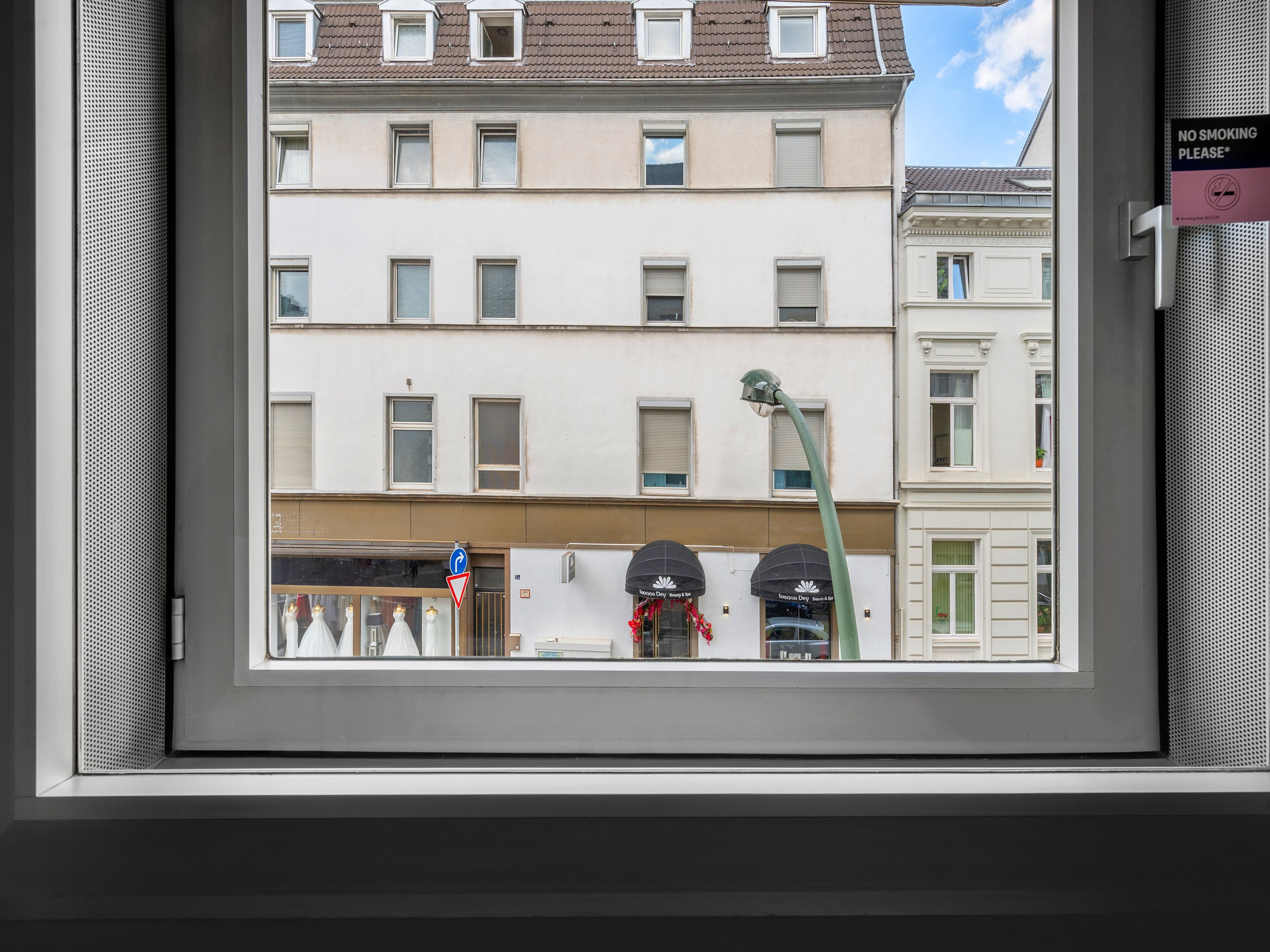 A view through a window of a building with multiple windows, a street lamp, and a no smoking sign.