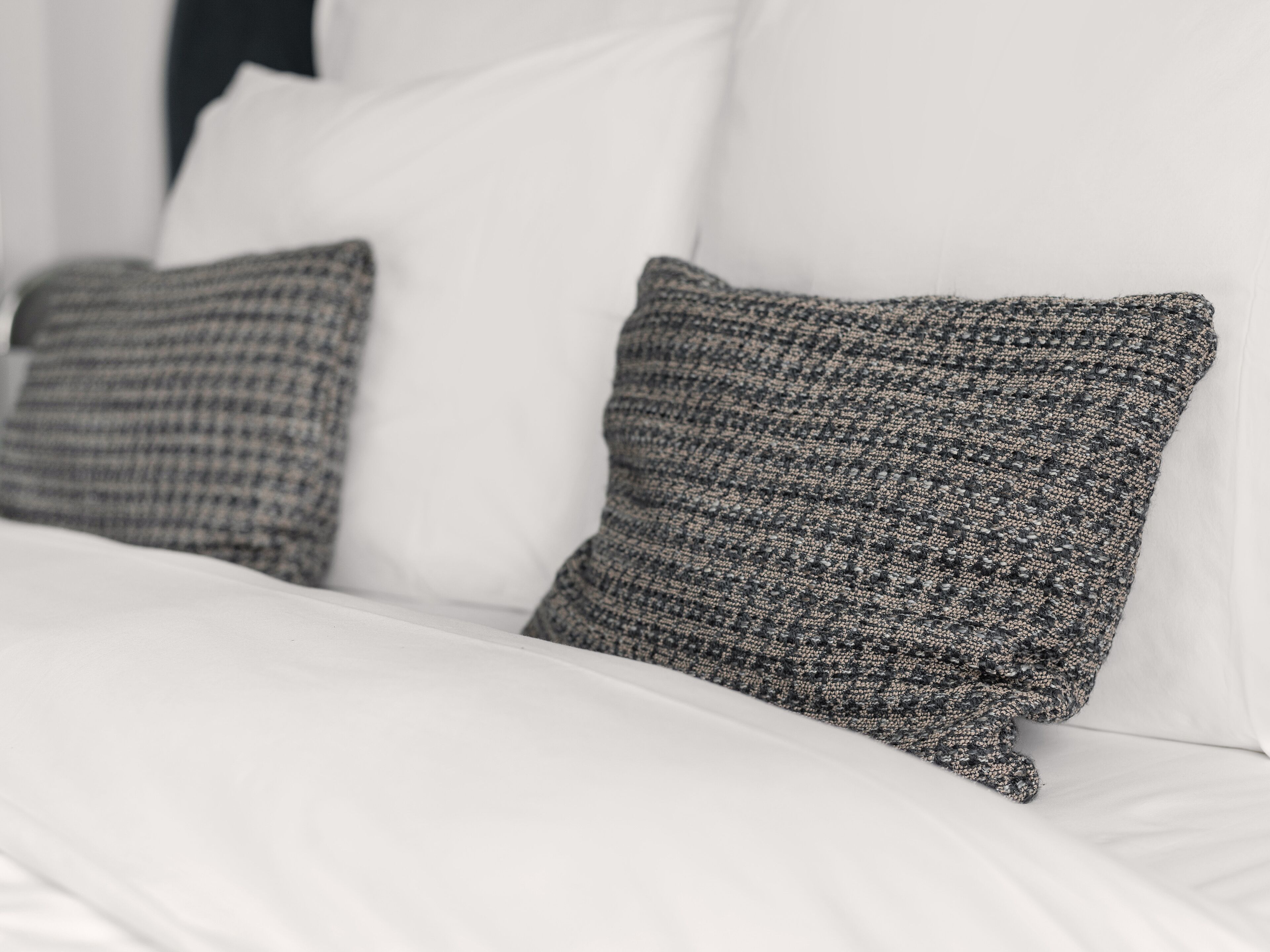 Un lit avec une literie blanche et deux oreillers gris à texture.