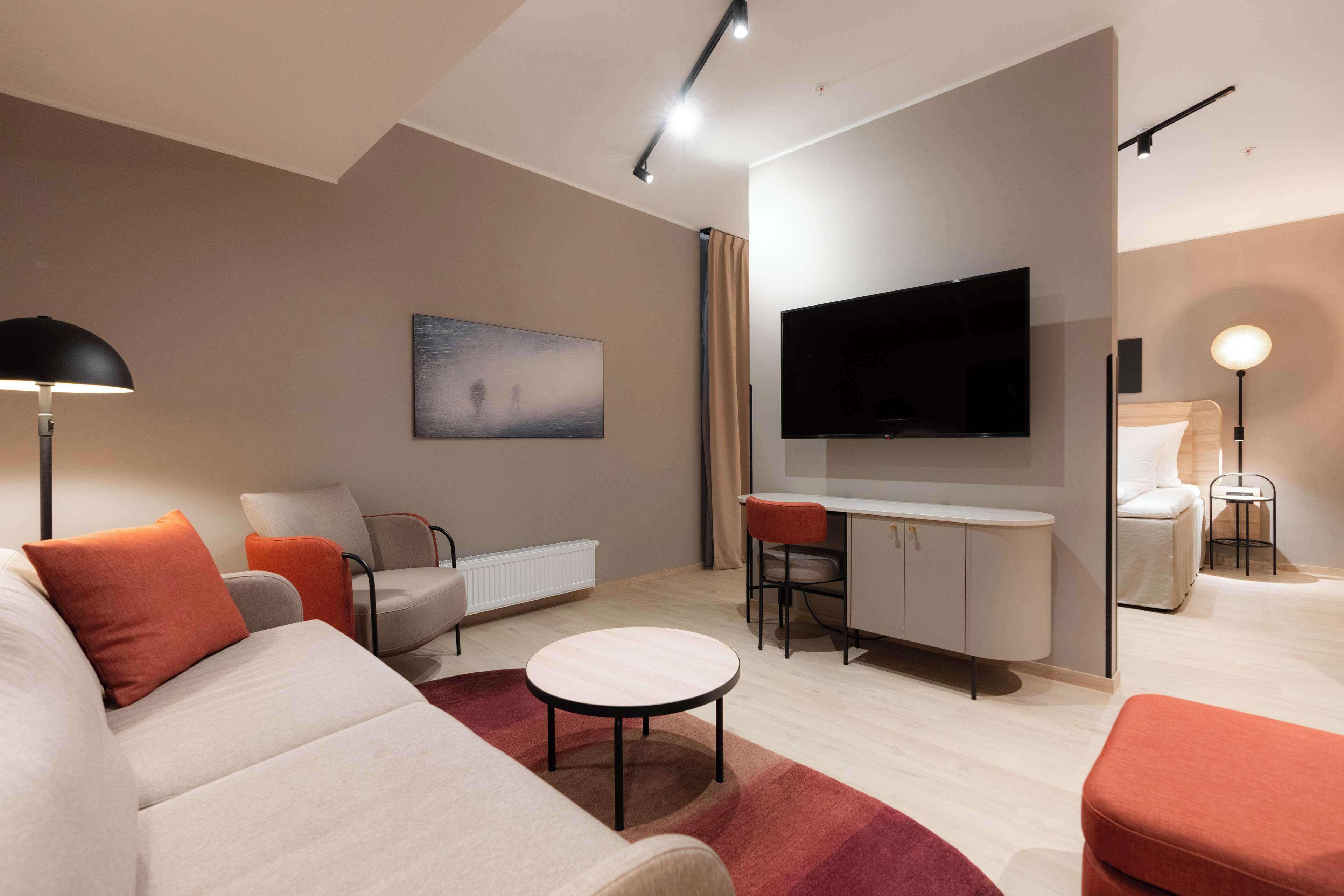 A modern living room with a sofa, chairs, a coffee table, a TV, and a desk area.