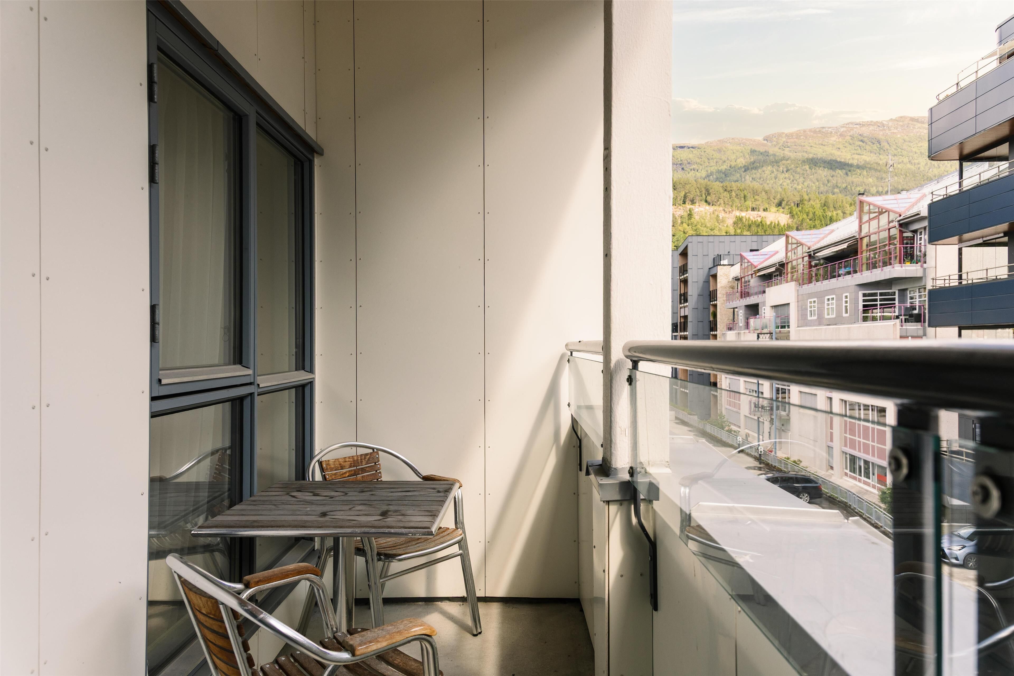 A balcony with a table and chairs, a view of buildings and hills in the background.