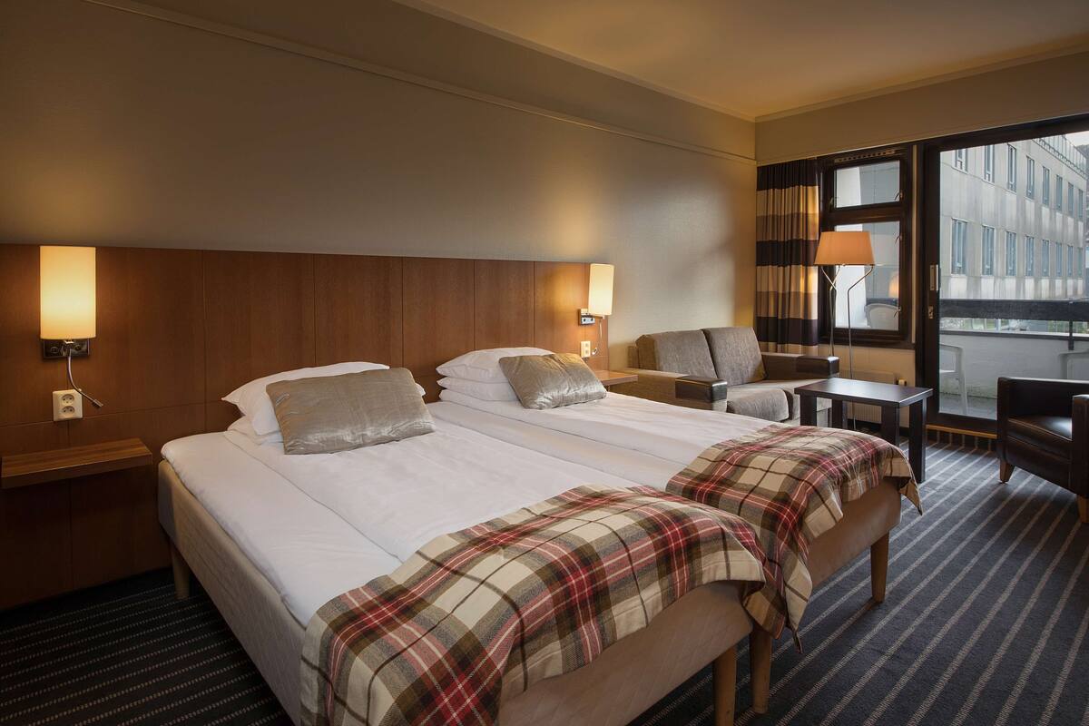 Ein Hotelzimmer mit zwei Betten, einem Schreibtisch, einem Stuhl und einem großen Fenster.