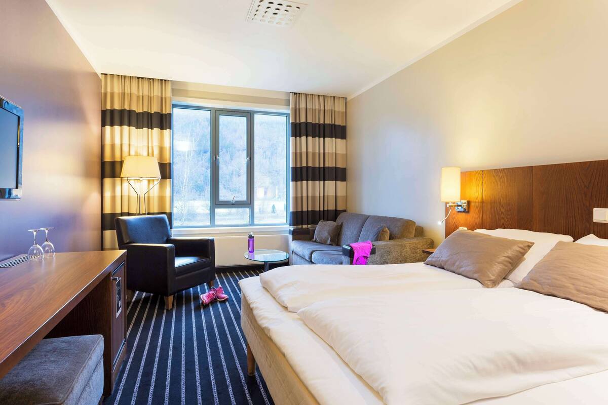 Ein Hotelzimmer mit einem großen Bett, einem Schreibtisch, einem Sessel, einer Couch und einem Fernseher.