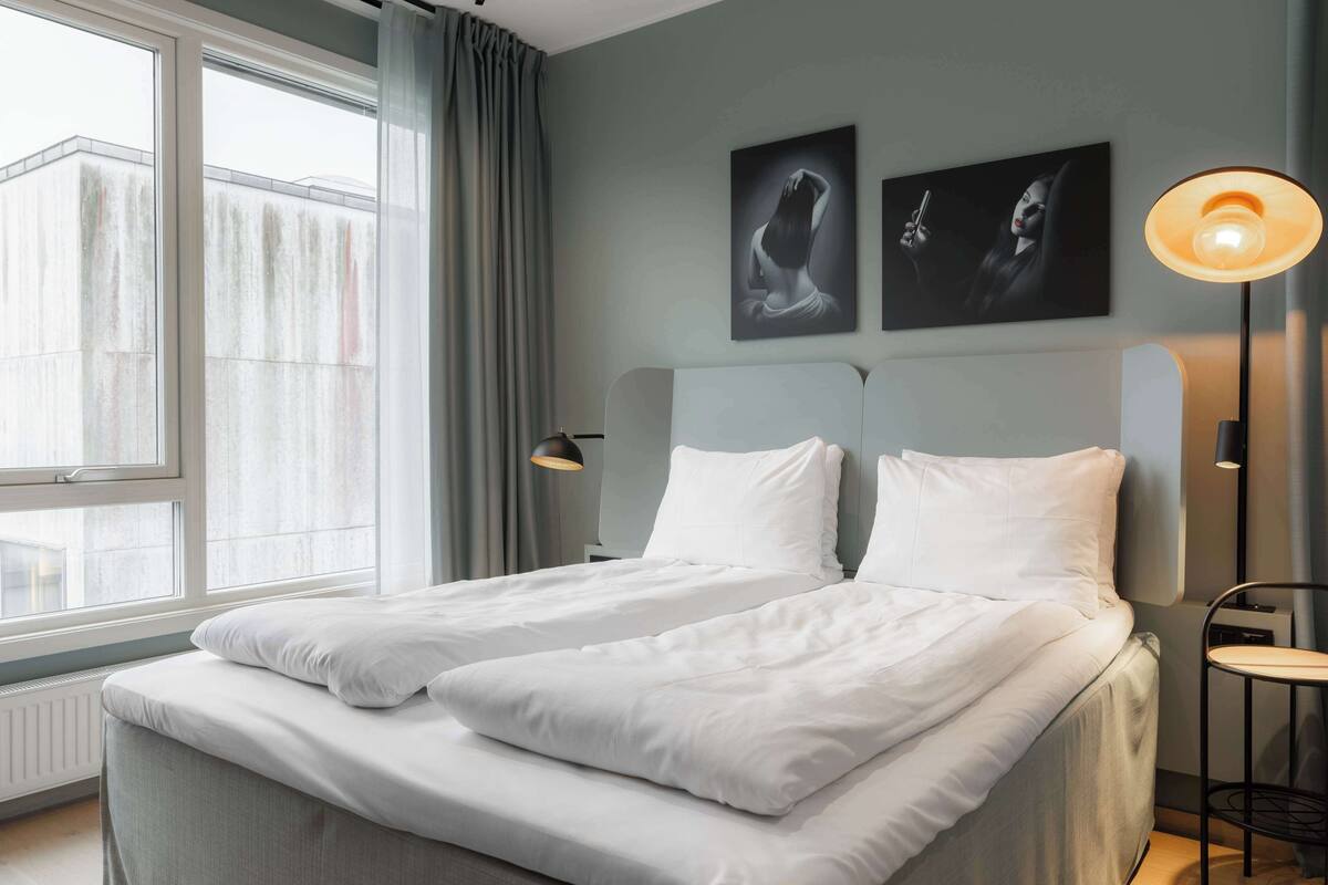 Ein modernes Hotelzimmer mit großem Fenster, zwei Betten, einem Nachttisch und einer Lampe.