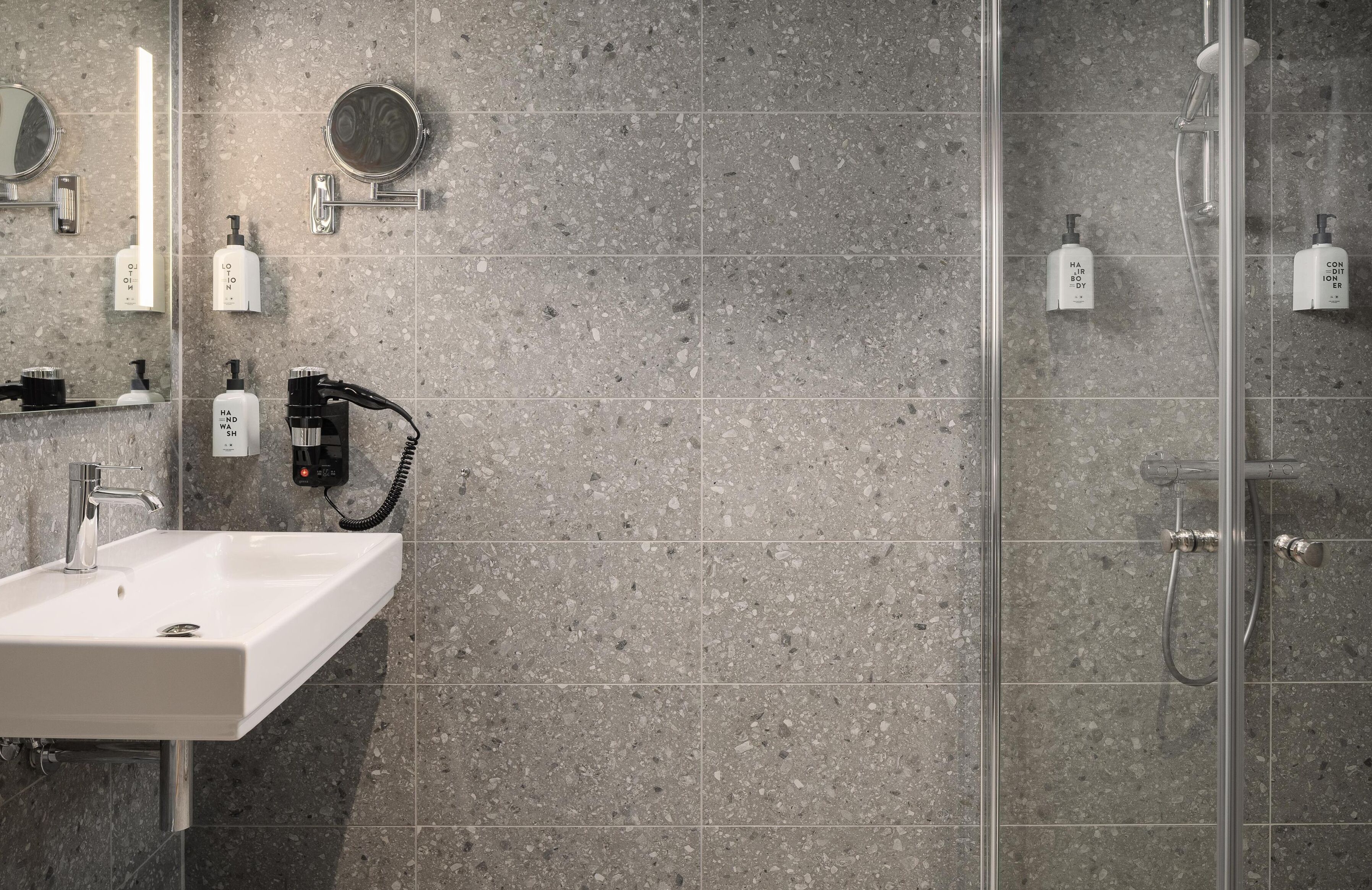 Un baño moderno con un lavamanos rectangular, un cabezal de ducha de mano y una zona de ducha con mampara de vidrio.