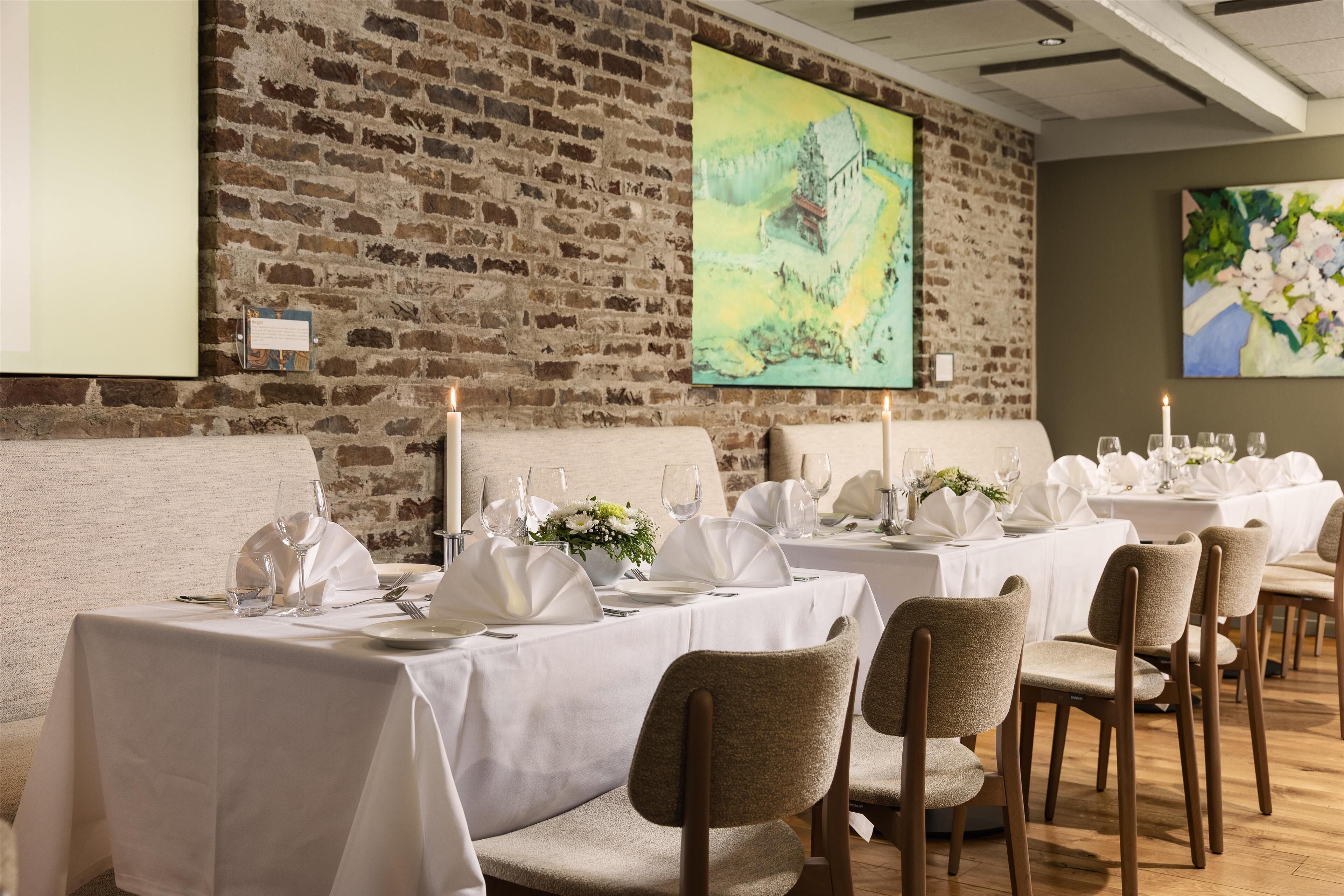 Un comedor con manteles blancos, mesas iluminadas con velas y un fondo de pared de ladrillo.
