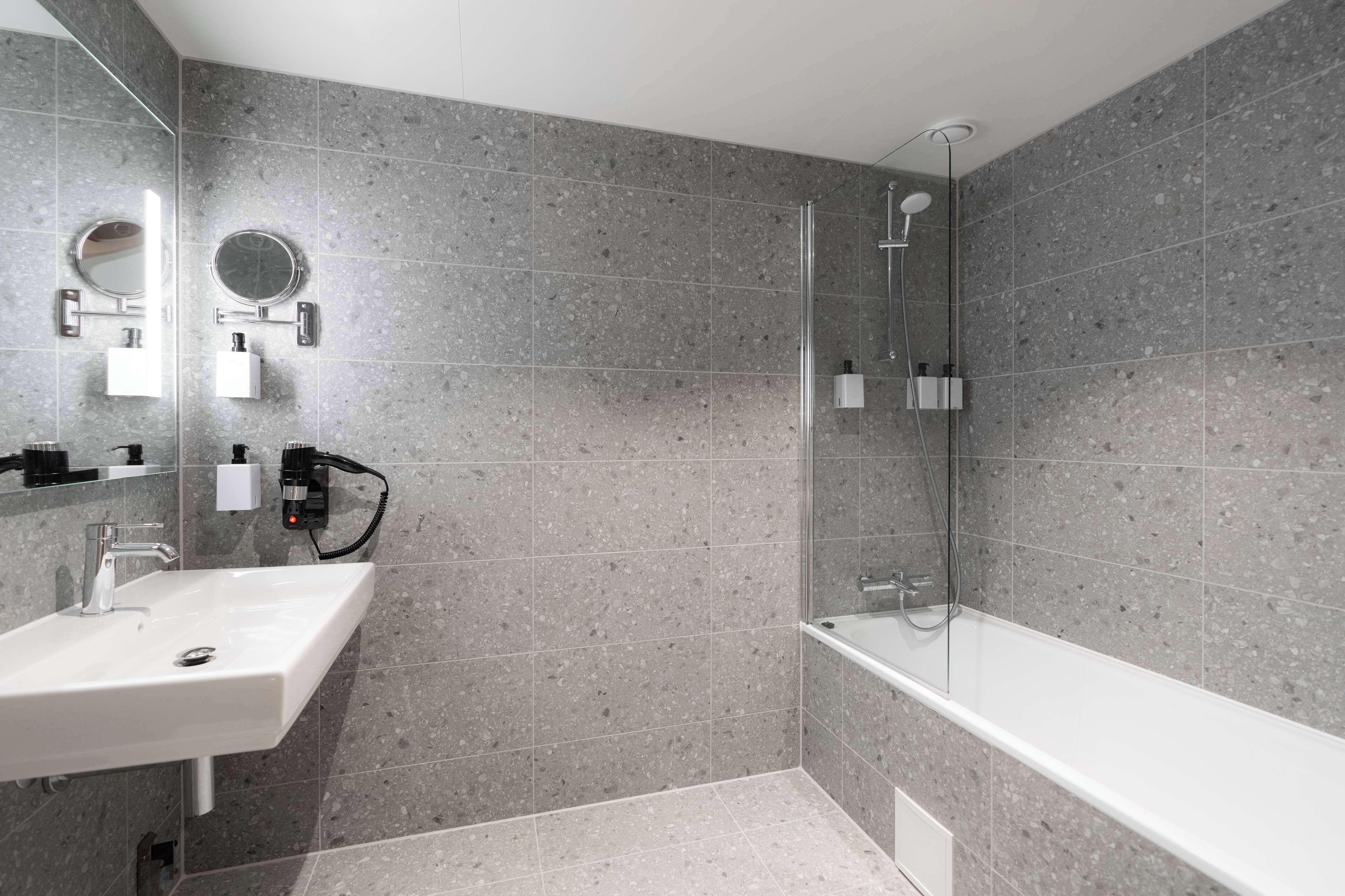 A modern bathroom with a white sink, a round mirror, and a glass-enclosed shower area.