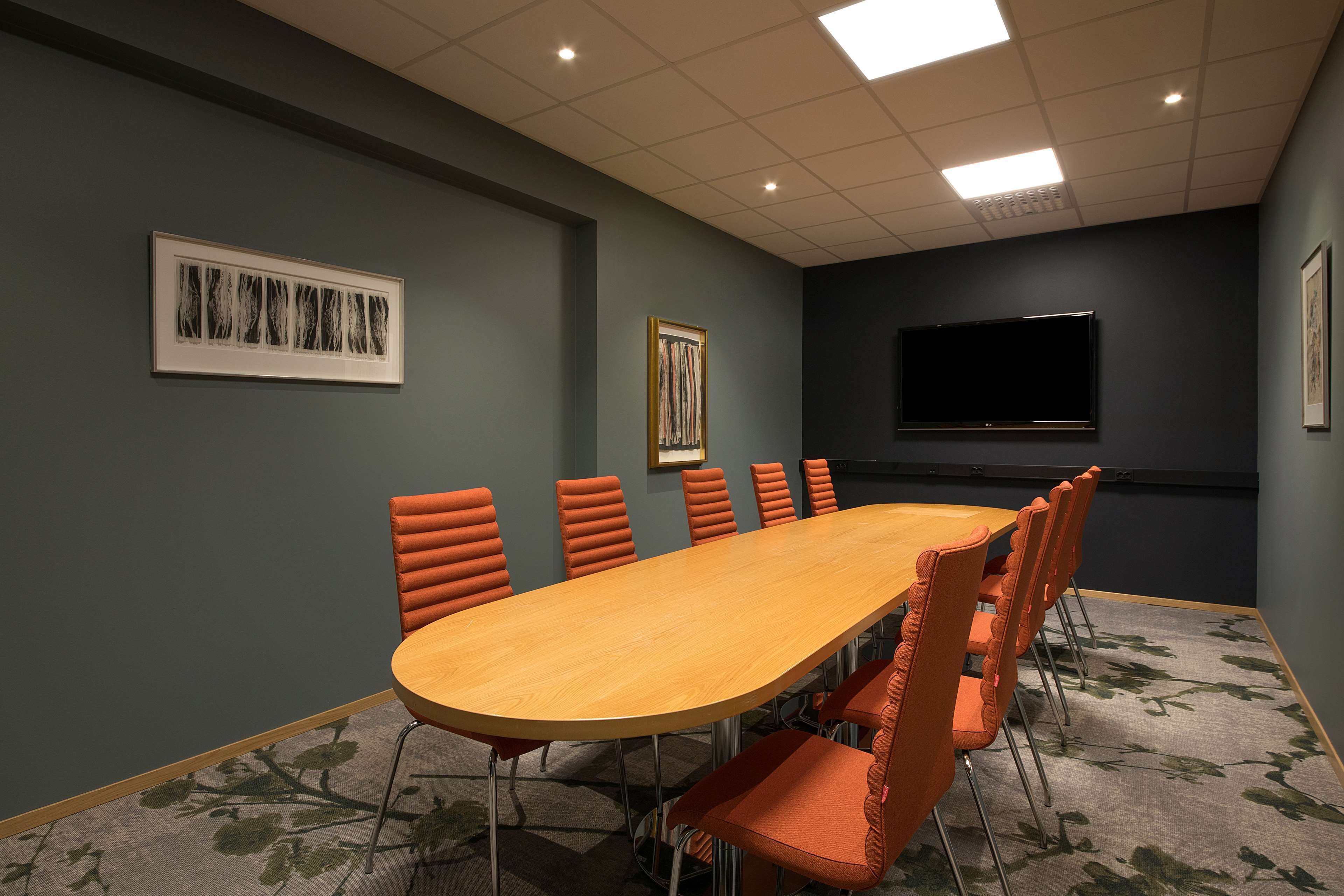 A conference room with a long wooden table, orange chairs, a flat-screen TV, and framed artwork on the walls.