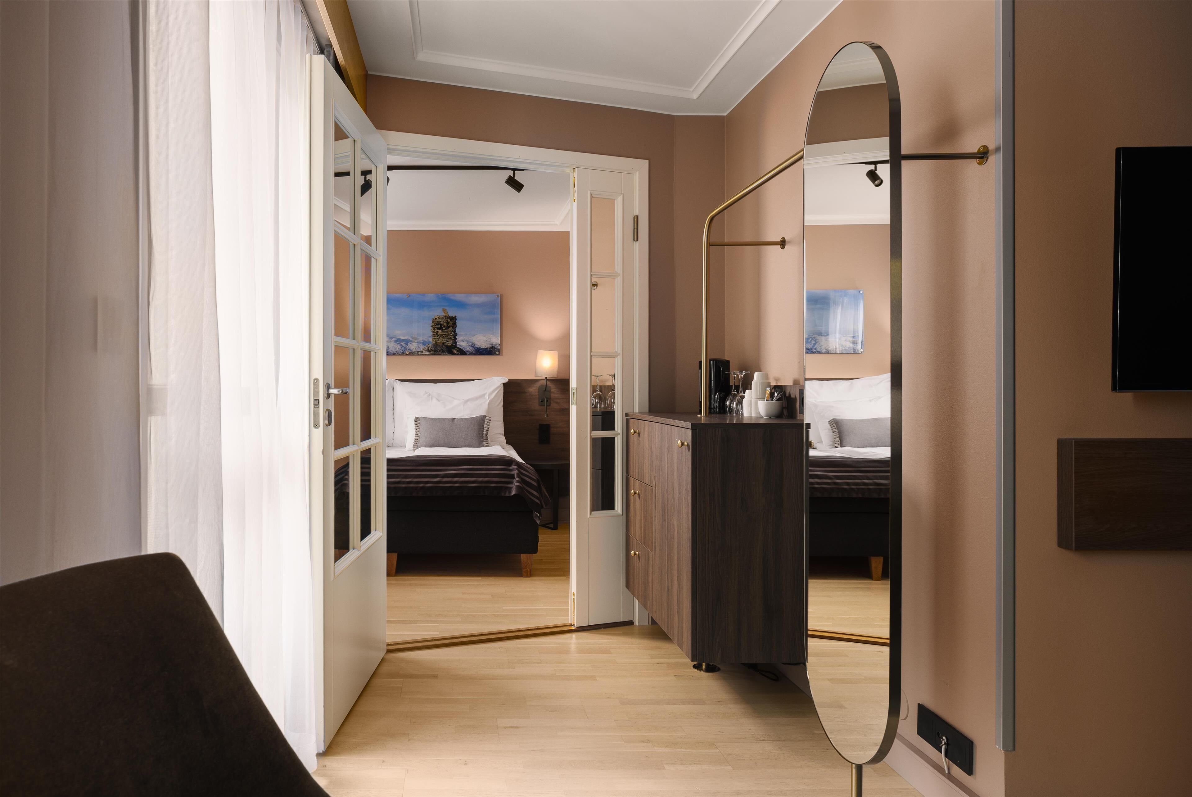 Ein Hotelzimmer mit Bett, Kleiderschrank, Spiegel und einer Tür zu einem anderen Raum.