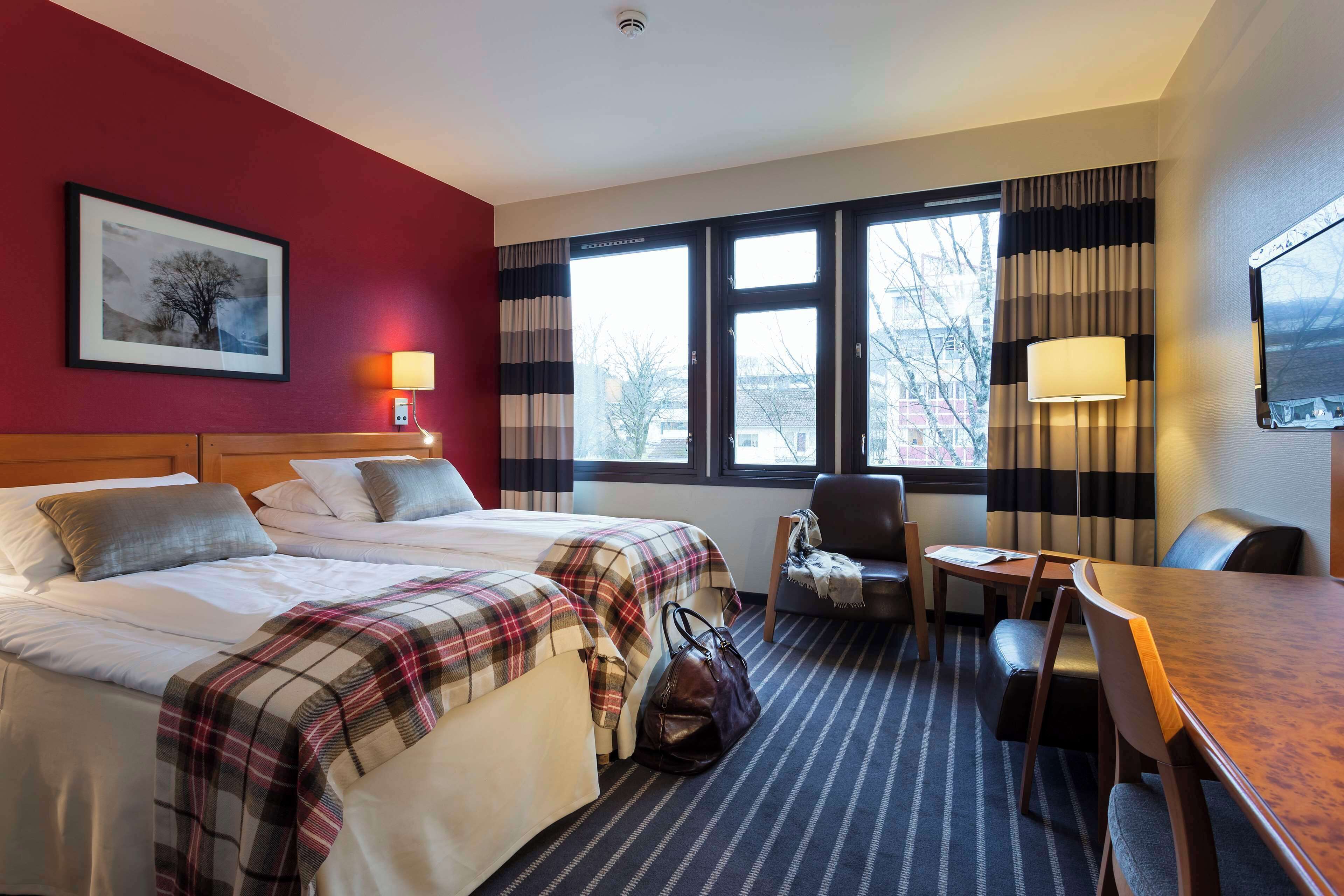 A hotel room with two beds, a desk, a chair, and a window with curtains.