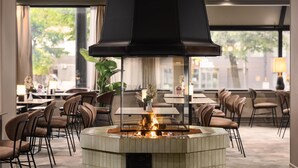 A modern dining area with a central fire feature, surrounded by chairs and tables.