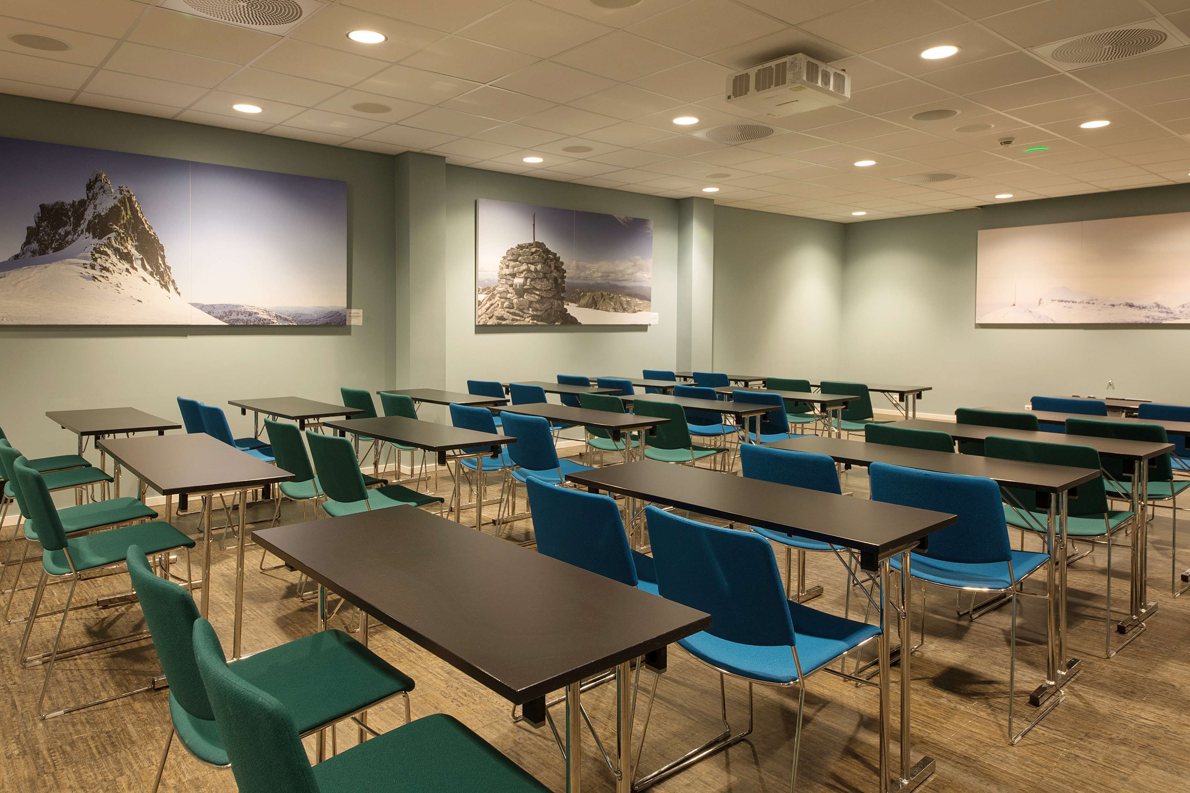 A conference room with tables and chairs, large wall art depicting mountains, and a wooden floor.
