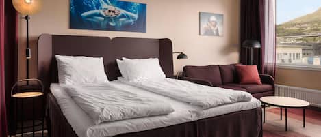 Una habitación de hotel con una cama grande, un sofá, una mesita y obras de arte en las paredes.