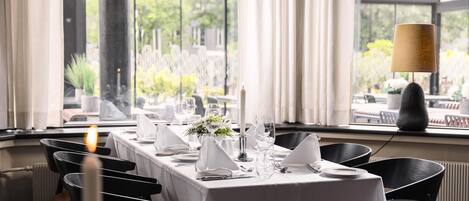 A dining table set for a meal with a candle, white tablecloth, and chairs.