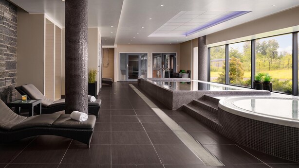 A modern indoor spa area with a hot tub, lounge chairs, and a view of the outdoors.