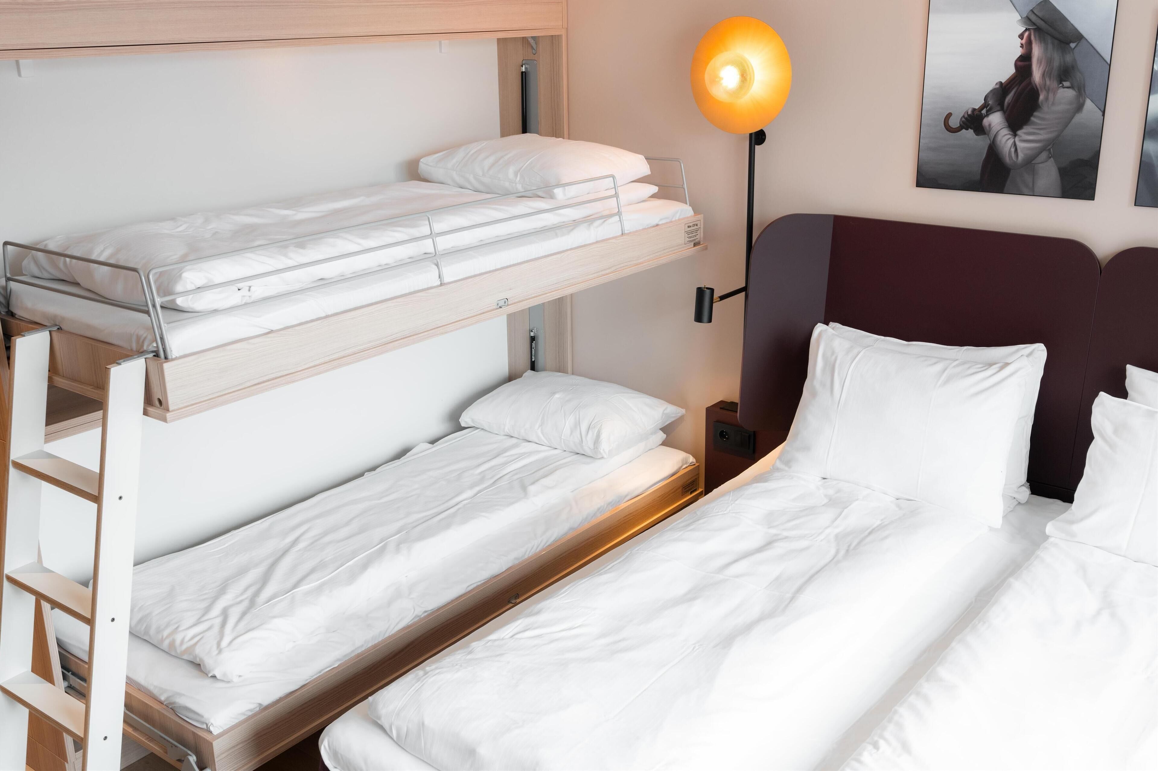 Habitación con literas, una escalera de madera, una mesita de noche con lámpara y ropa de cama blanca.