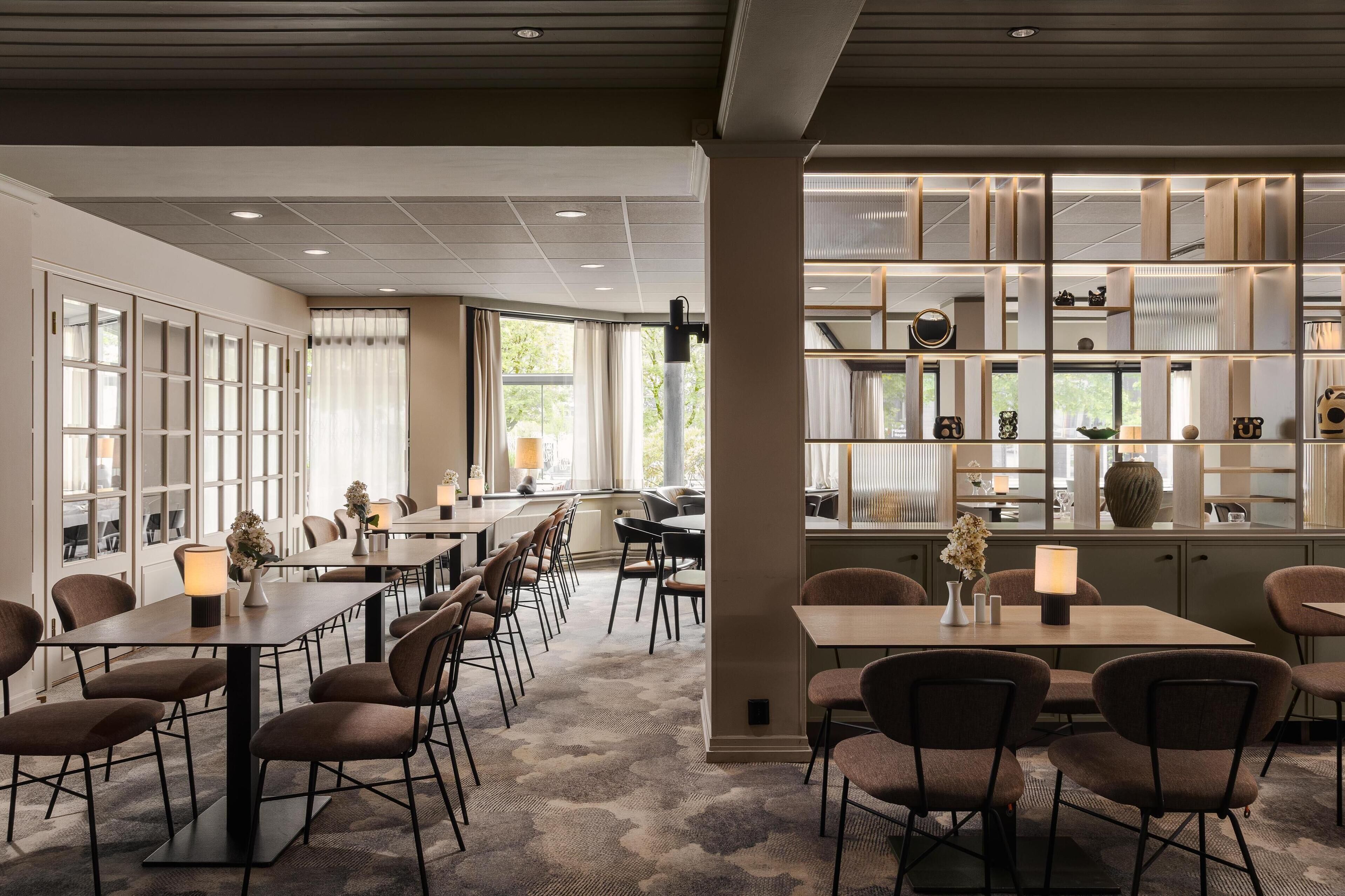 A modern hotel dining area with long tables, chairs, and a decorative wall with shelves.