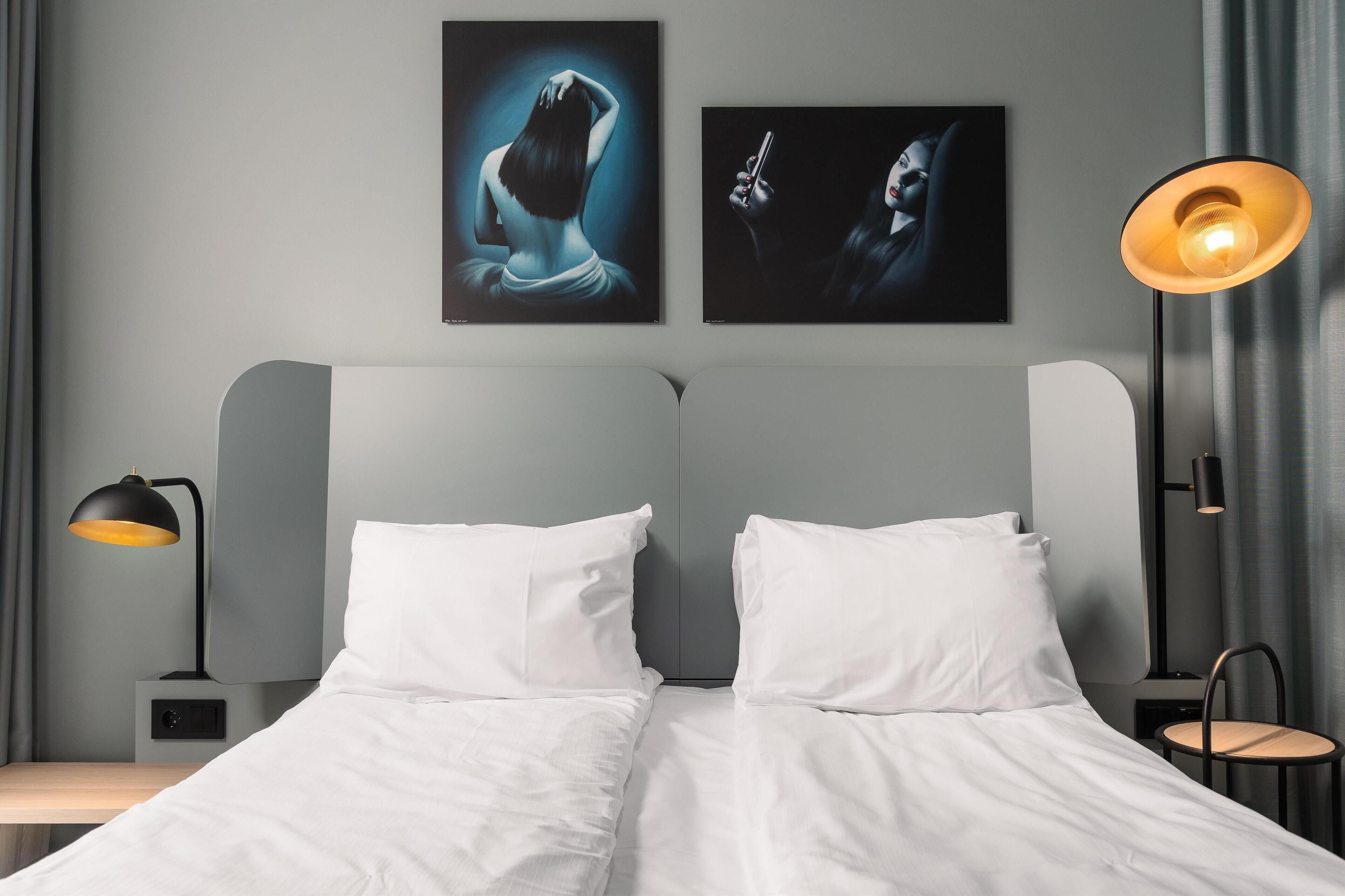 A modern hotel room with a bed, two bedside tables, a chair, and artwork on the wall.