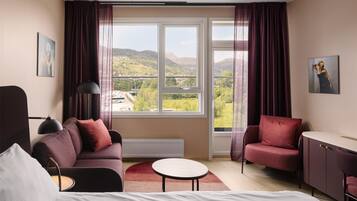 A modern hotel room with a large window, a sofa, a desk, and a bed.