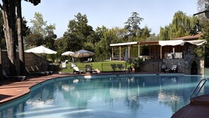 A swimming pool with lounge chairs and umbrellas, surrounded by trees and a stone building. - Hotel Villa Stanley (Sesto Fiorentino)