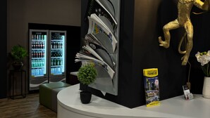 A reception desk with a magazine rack, a small potted plant, a guidebook, and a decorative golden figure. - Colour Hotel (Frankfurt)