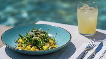 Un plato azul con ensalada y un vaso de limonada junto a una piscina.