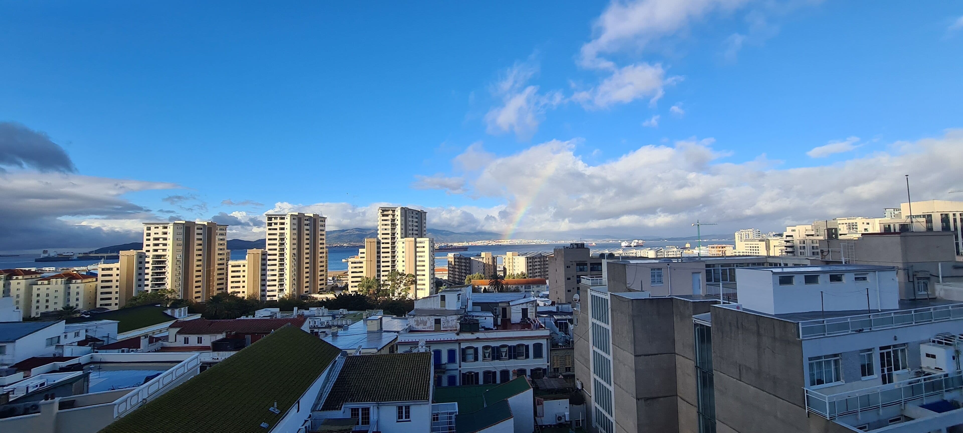 Un paisaje urbano con edificios altos, cielo despejado y un arcoíris distante.