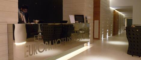 A hotel reception desk with a modern design, a digital screen, and a seating area with chairs.