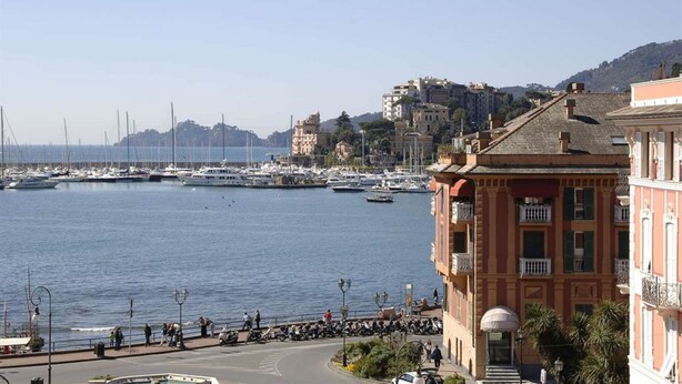 Marina costeira com barcos, um calçadão e edifícios com varandas.