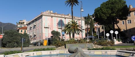 Una piscina con una escultura de pulpo en el centro, rodeada de vegetación y un edificio de fachadas rosas y blancas al fondo.