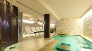 Piscina interior com espreguiçadeiras e uma parede de pedra.