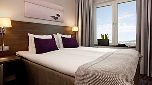 Habitación de hotel con una cama grande, dos mesitas de noche, una ventana con cortinas y vistas al cielo.
