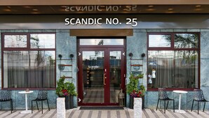 La entrada a Scandic No. 25 con puerta de cristal, dos plantas en macetas y zona de estar al aire libre.