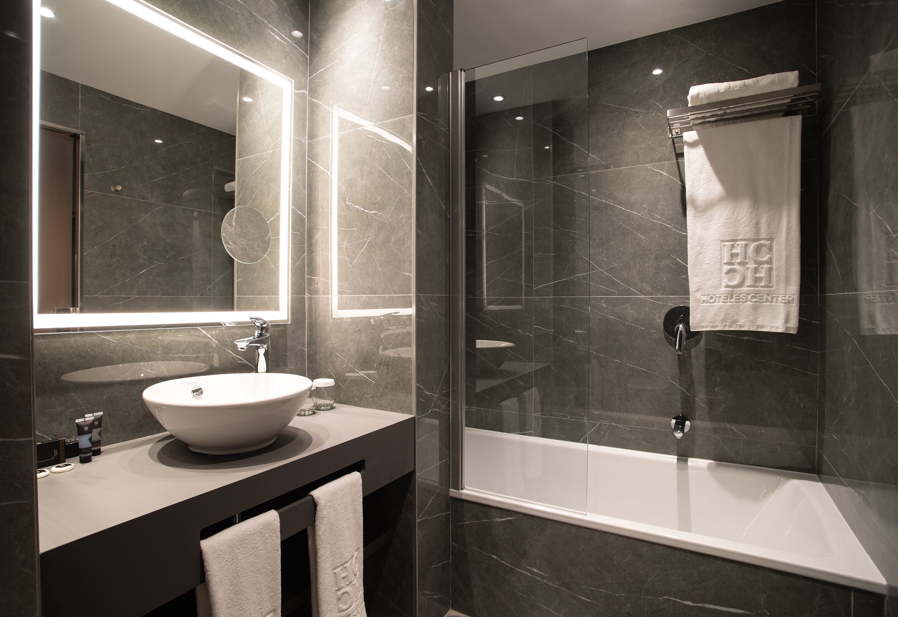 A modern bathroom with a large mirror, a round sink, a bathtub, and a glass-enclosed shower area.