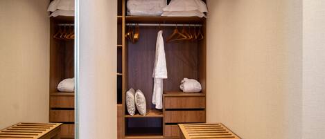 A walk-in closet with wooden shelves, a hanging rack, and a bench.