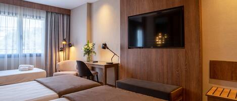 Ein Hotelzimmer mit zwei Betten, einem Schreibtisch, einem Stuhl, einem Fernseher und einem kleinen Tisch.