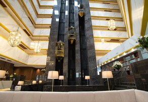 A modern lobby with marble floors, a central staircase, and multiple chandeliers.