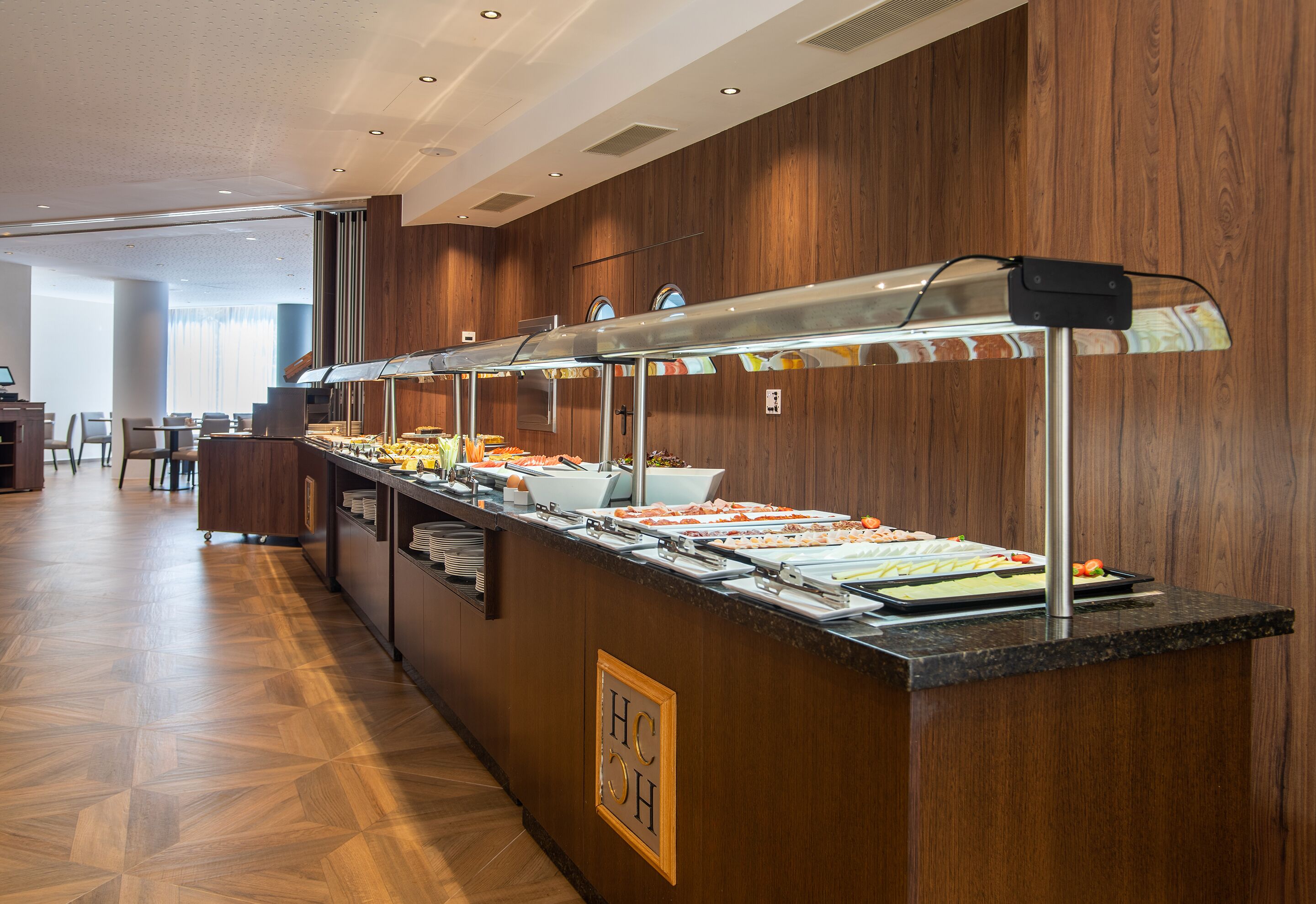 A buffet area with multiple food stations, a wooden wall, and a seating area in the background.