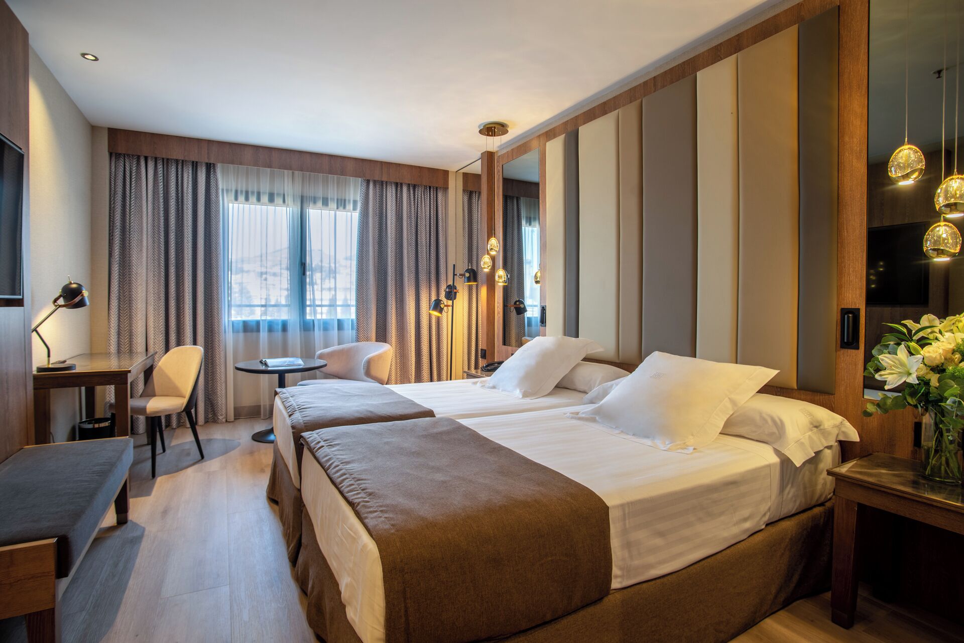 A hotel room with two beds, a desk, a chair, and a small table.