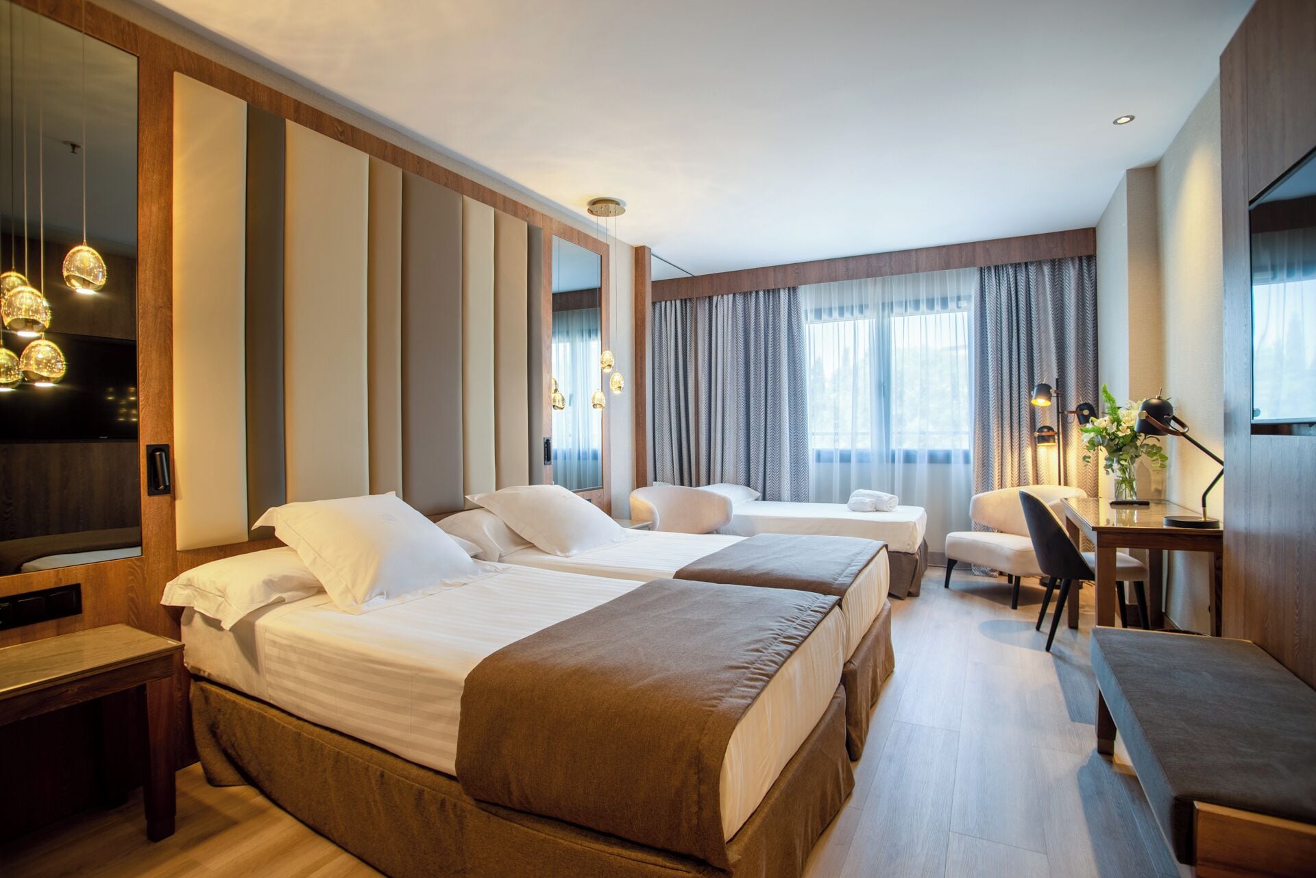 A hotel room with two beds, a desk, a chair, and a large mirror.