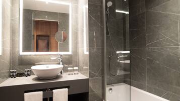 Un baño moderno con un espejo grande, un lavamanos blanco y una ducha con paredes de vidrio.