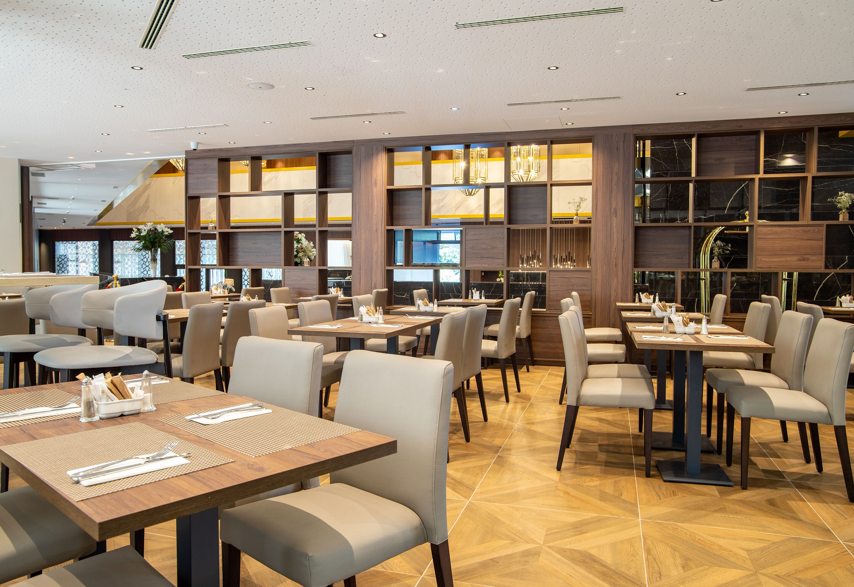 A modern restaurant with multiple dining tables and chairs, wooden paneling, and a patterned floor.