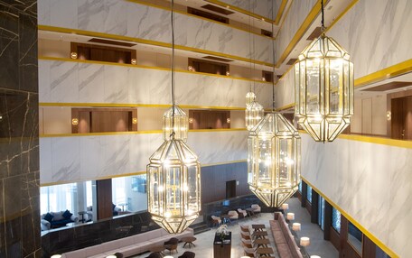 A spacious lobby with a long reception desk, multiple seating areas, and hanging geometric chandeliers.