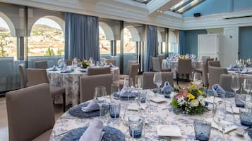 A dining area with round tables set for a meal, featuring blue glassware and floral centerpieces.