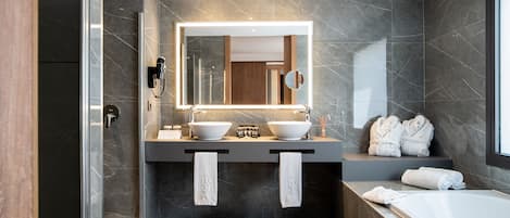 A modern bathroom with two sinks, a large mirror, and a bathtub.