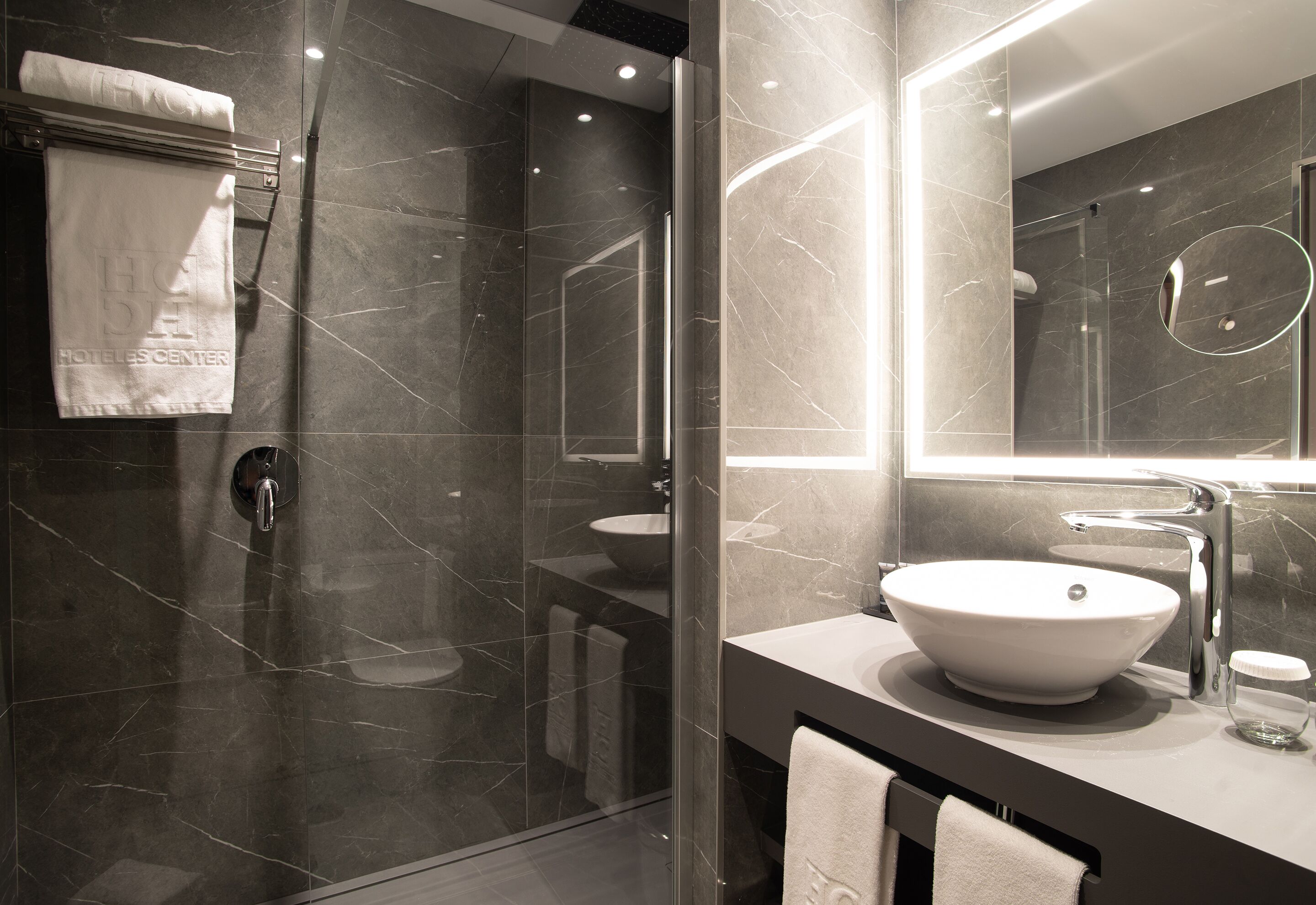 Un baño moderno con ducha envuelta en vidrio, un espejo grande y un lavabo sobre encimera.